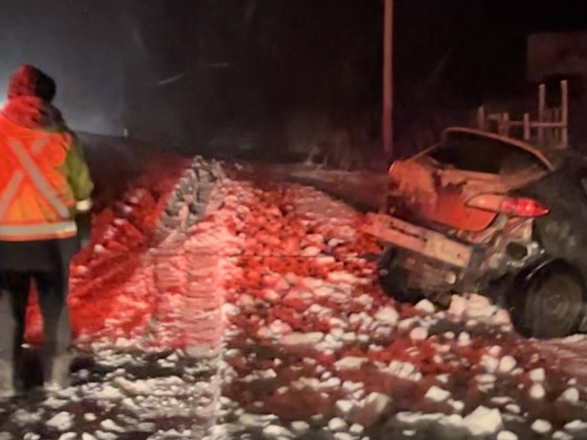 Tow operator in a high-visibility vest beside a damaged car on a snowy road at night